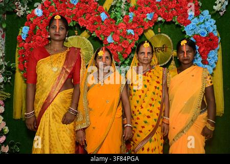Young indian man with three women in yellow sarees with haldi tilak posing together smiling in front of red blue rose heart backdrop during haldi cere Stock Photo