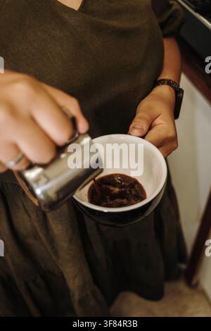 Fresh espresso being poured into a ceramic cup before adding steamed milk. Preparing a handcrafted specialty coffee beverage. Stock Photo