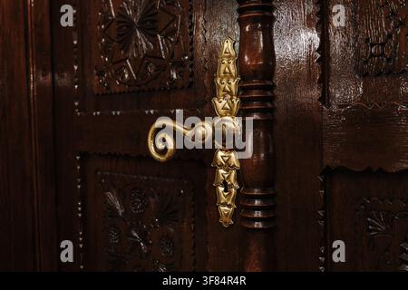 Decorative brass handle mounted on an intricately carved wooden door. Traditional craftsmanship and historic architectural details. Stock Photo