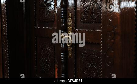 Decorative brass handle mounted on an intricately carved wooden door. Traditional craftsmanship and historic architectural details. Stock Photo