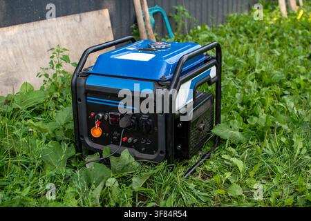 Blue portable gasoline power generator standing in green grass outdoors Stock Photo