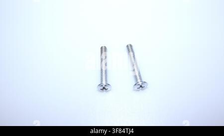 Two small metal screws isolated on white background for furniture assembly, repair, installation, woodworking, and DIY projects. Stock Photo