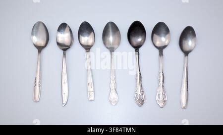 Assorted metal teaspoons arranged in a row isolated on white background for kitchen, dining, coffee, tea, and tableware concepts. Stock Photo