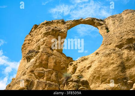 A large, natural sandstone rock formation featuring a prominent circular hole or arch in its center. The rough, tan-colored rock is textured with crac Stock Photo
