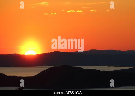 Colorful sunset with glowing orange and red clouds above a dark silhouetted landscape. Stock Photo