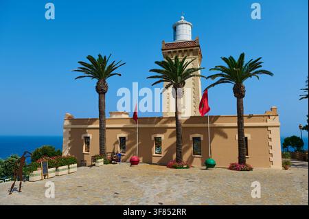 Tangier, Morocco - the 28th of July 2026 Sunlit lighthouse framed by palm trees on a paved seaside terrace overlooking the blue Atlantic with flags an Stock Photo