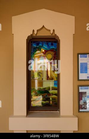 Tangier, Morocco - the 28th of July 2026 Colorful stained-glass window depicting a lighthouse, sun and palm set in a decorative architectural frame, s Stock Photo