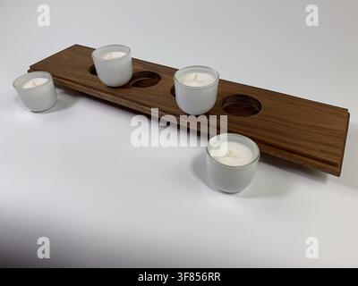 Long wooden plank candle holder with four white ceramic cups, one candle lit, on a white background. Stock Photo