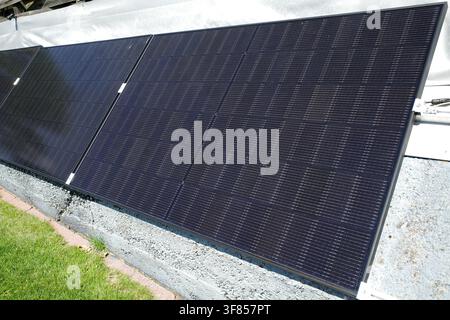 Solar panels mounted on a textured, light-colored concrete wall. The panels have a dark surface with a grid-like pattern, efficiently absorbing sunlig Stock Photo