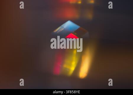 Small glass prism casting red yellow and blue refracted light on dark surface for abstract optical background Stock Photo
