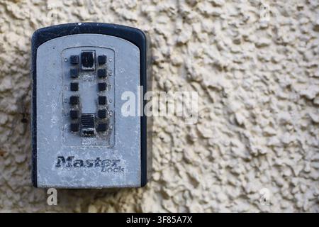 Weathered combination key lock box mounted on a rough stone wall, showing numbered buttons and a secure access mechanism. Stock Photo