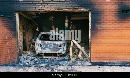 A burnt out car and destroyed garage inside a damaged brick building following shelling and fire caused by war conflicts Stock Photo