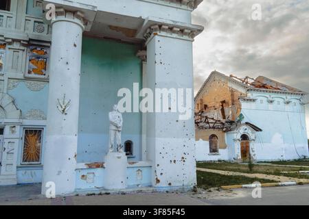 Damaged heritage building with shrapnel marks on white columns and standing statue after military shelling during armed conflict Stock Photo
