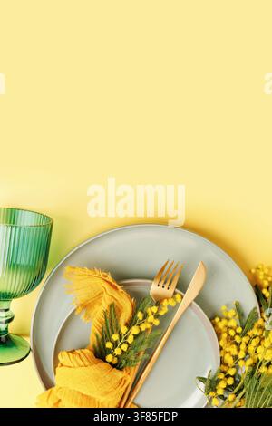 Modern spring decor with mimosa and stylish glassware on yellow background Stock Photo