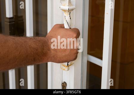Adult hand pulling old door handle, opening a gate or entrance Stock Photo