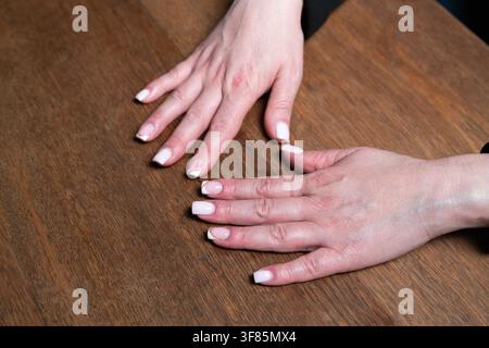 Close-up of woman's hands with elegant French manicure gently touching on a warm wood table. Stock Photo