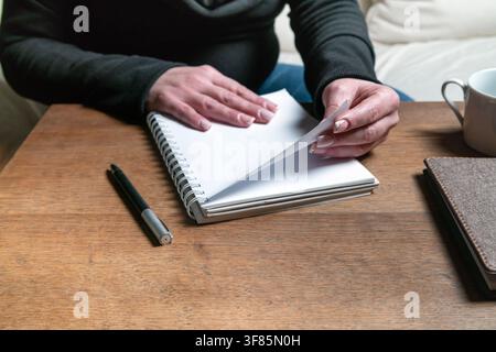 A woman's hands turning a page in a blank spiral-bound planner, next to a pen and a cup of coffee Stock Photo