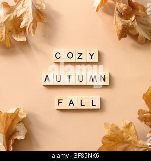 Golden dry oak leaves as border and wooden blocks with letters and text - Fall, Cozy, Autumn. Autumn concept on beige background. Stock Photo