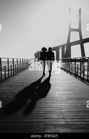 Couple silhouetted enjoying romantic walk on a lisbon pier Stock Photo