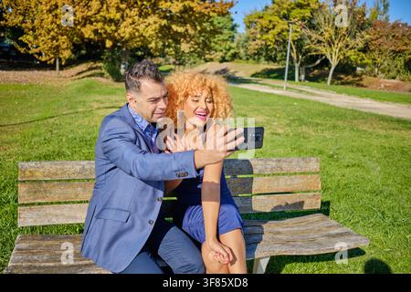 Diverse couple enjoying a happy moment together, taking a selfie outdoors in a park Stock Photo
