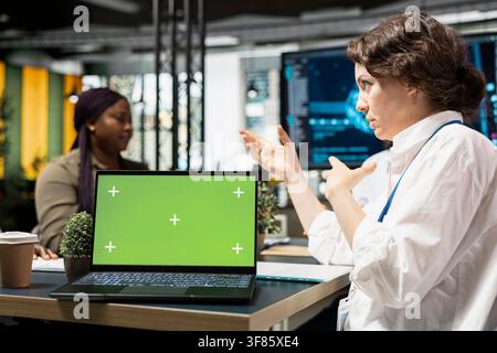 Green screen laptop used by computer scientists developing AI software, designing coding solutions together. Teamworking colleagues optimizing technical performance with mockup notebook Stock Photo