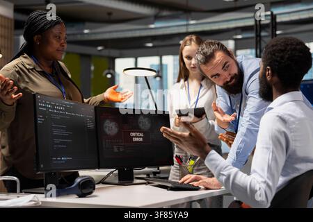 Team of technicians working together to fix critical error warning popup in office. IT staff members doing brainstorming, troubleshooting glitch notification on PC screen Stock Photo