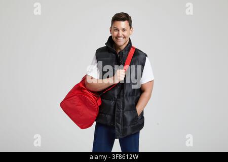 An unnamed man carries a red duffel bag by its shoulder strap in a studio setting in London, England, United Kingdom, on 17 March 2017. Stock Photo