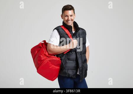 An unnamed man holds a red duffel bag by the strap in a studio setting in London, England, United Kingdom, on 17 March 2017. Stock Photo