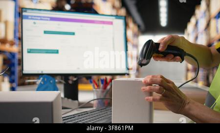 Asian employee applying shipping labels and scanning tracking info, registering the cargo information for parcel status during delivery. Manages labeling tasks with hi vis vest in depot. Camera A. Stock Photo