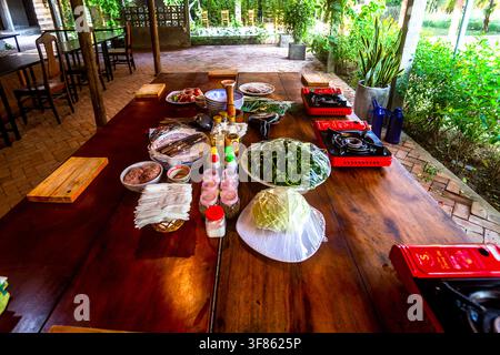 A long wooden table with food and burners set up to teach cooking at a resort in SE Asia. Cooking school. Stock Photo