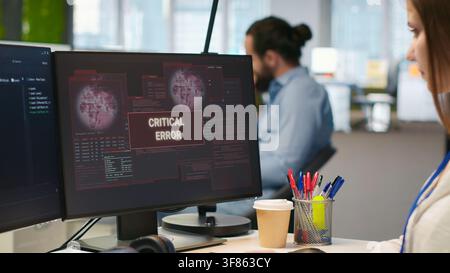 Female engineer in startup office struggling to fix critical error warning popup. Intern doing maintenance on computer glitches while coding in software development agency, camera A Stock Photo