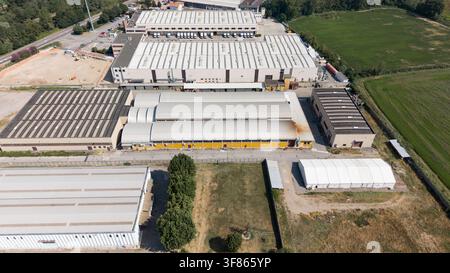 Aerial view of a modern warehouse complex with industrial buildings, loading docks, surrounding roads, and green fields in Zibido San Giacomo, Lombard Stock Photo