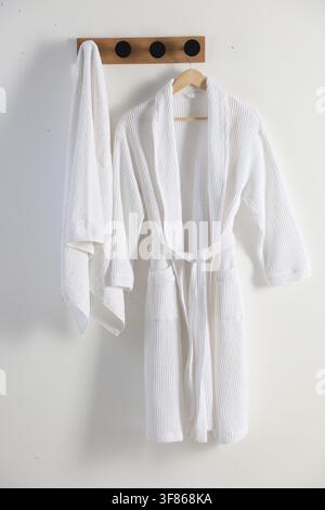 Clean cotton bathrobe and towel on white wall Stock Photo