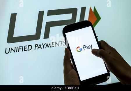 In this photo illustration, A person uses a smartphone displaying the G Pay logo against a prominent UPI, Unified Payments Interface, backdrop, illust Stock Photo