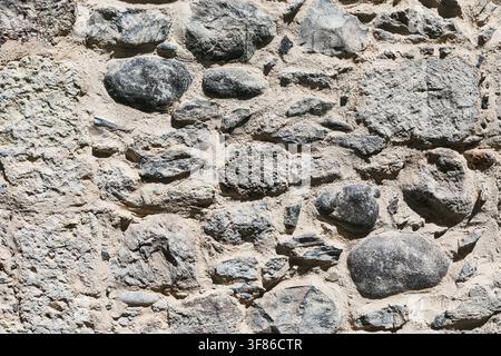 Ancient dry stone wall built from irregular rounded and flat rocks set in mortar, showing centuries of weathered texture. Textured stone or concrete w Stock Photo