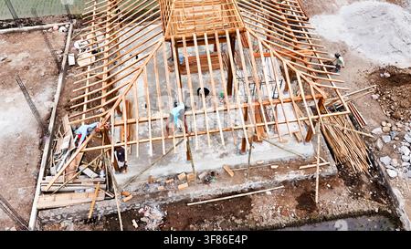 Aerial view of the construction progress of a traditional Javanese Joglo house featuring wooden roof framing and workers on site in Kecamatan Tingkir, Stock Photo