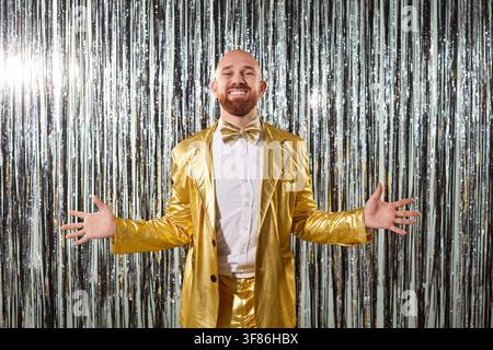 Party happy man, sparkly silver backdrop bright lights, funny man wearing shiny gold suit, bow tie  Stock Photo