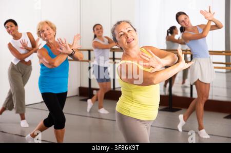 Portrait of mature woman practicing ballet dance moves during group class in choreographic studio Stock Photo