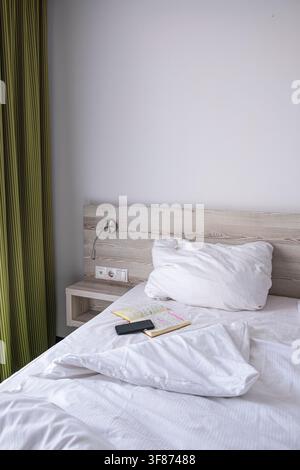 View of a hotel bed with a smart phone and a note book on it, creating a cozy morning routine atmosphere. Stock Photo