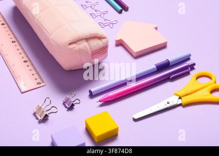 School supplies and stationery items including a pink pencil case, pens, ruler, and scissors on a purple background Stock Photo