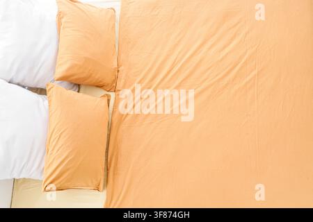 Top down view of a bed with two white pillows and two orange pillows on a light orange sheet, comfortable bedding Stock Photo