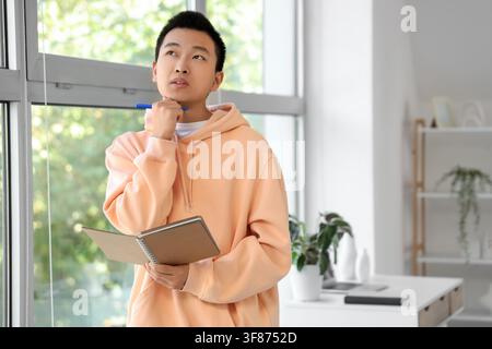 Thoughtful young Asian man with notebook at home Stock Photo
