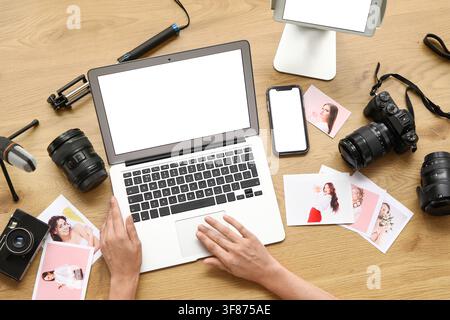 Overhead view of a photographer editing images on a laptop with camera gear and printed photos on a wooden desk Stock Photo