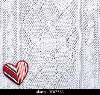 Wool sweater texture of white color with cable knitting stitch pattern and heart-shaped textile patch. Natural knitted wool white material with orname Stock Photo