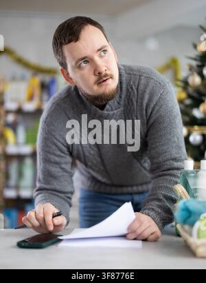 Middle-aged man restocking using paper in store with New Year decoration Stock Photo