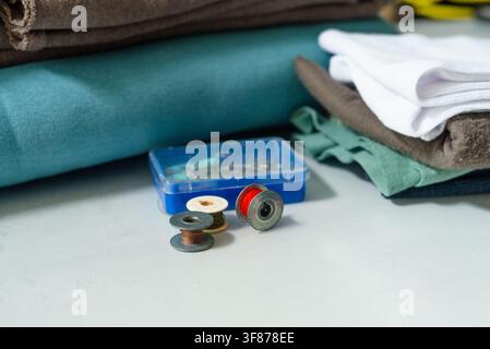 Thread spools organized in blue container on white sewing table. Sewing supplies and accessories arranged for colorful crafting hobby. Creative sewing essentials displayed for productive textile work Stock Photo