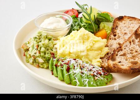 Cafe brunch plate with scrambled eggs, toasted sourdough bread, fresh salad and dipping sauce served on a white oval plate on a light gray background, Stock Photo