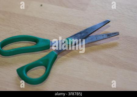 light duty green handle paper scissors on a fake wood kitchen surface super close-up with shallow depth of field Stock Photo