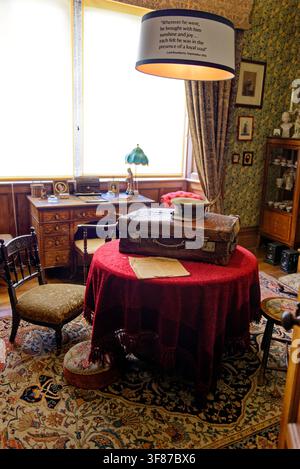 A beautifully preserved historic room featuring an antique leather suitcase on a red tablecloth, an executive desk by the window, and patterned textil Stock Photo