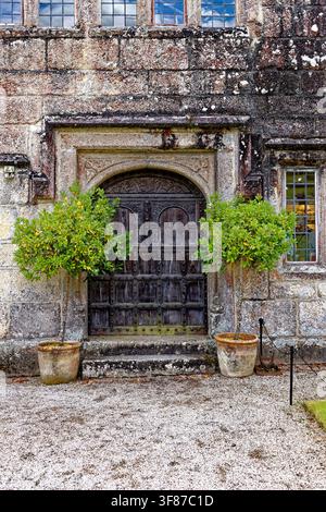 A beautifully detailed historic entrance featuring heavily carved double oak doors, a stone lintel archway, weathered granite masonry, and flanking po Stock Photo
